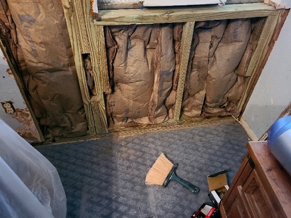 A room with walls being remodeled and the floor is covered in insulation.